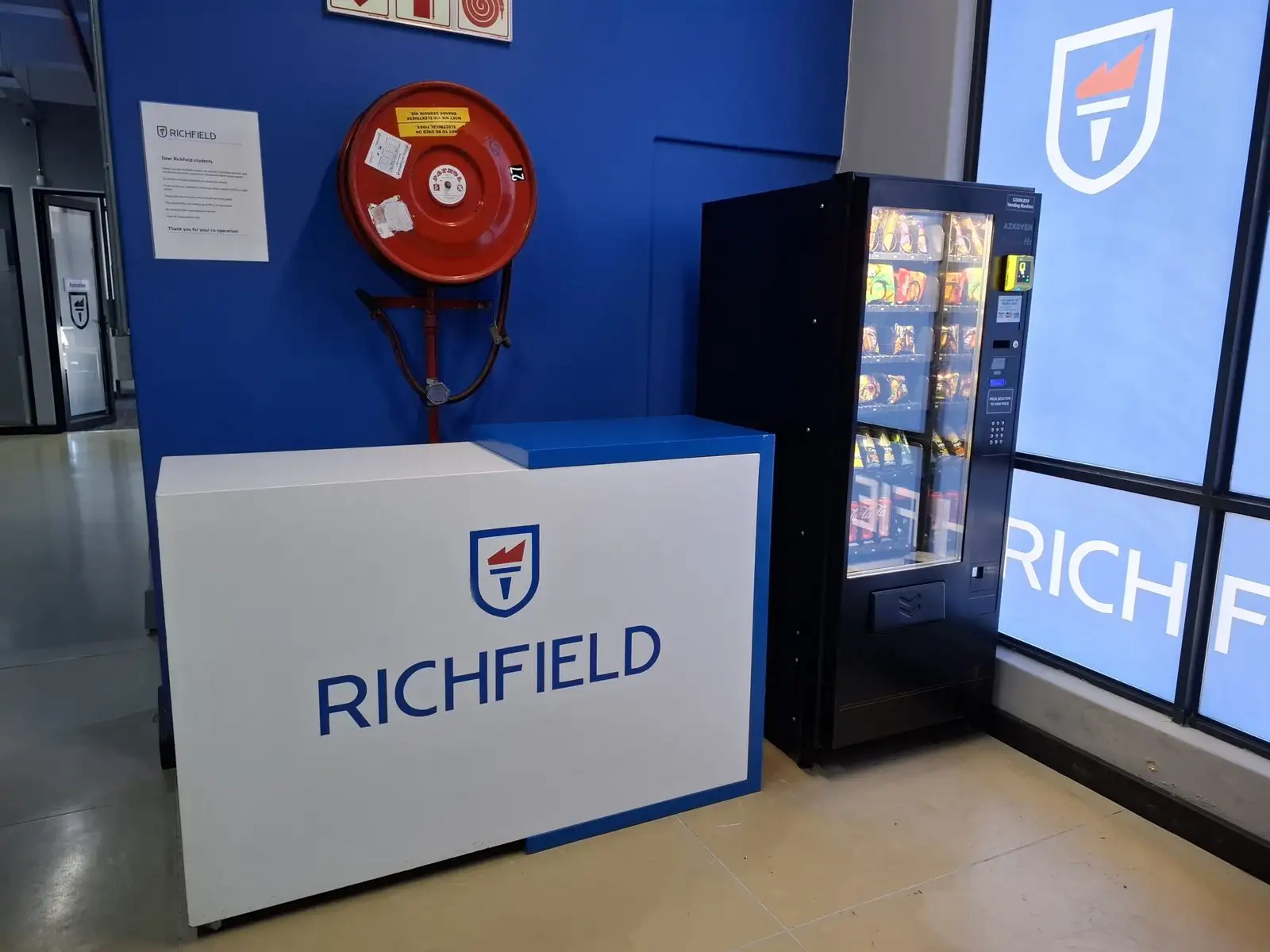 A Richfield-branded vending machine installed beside a reception desk at a college campus