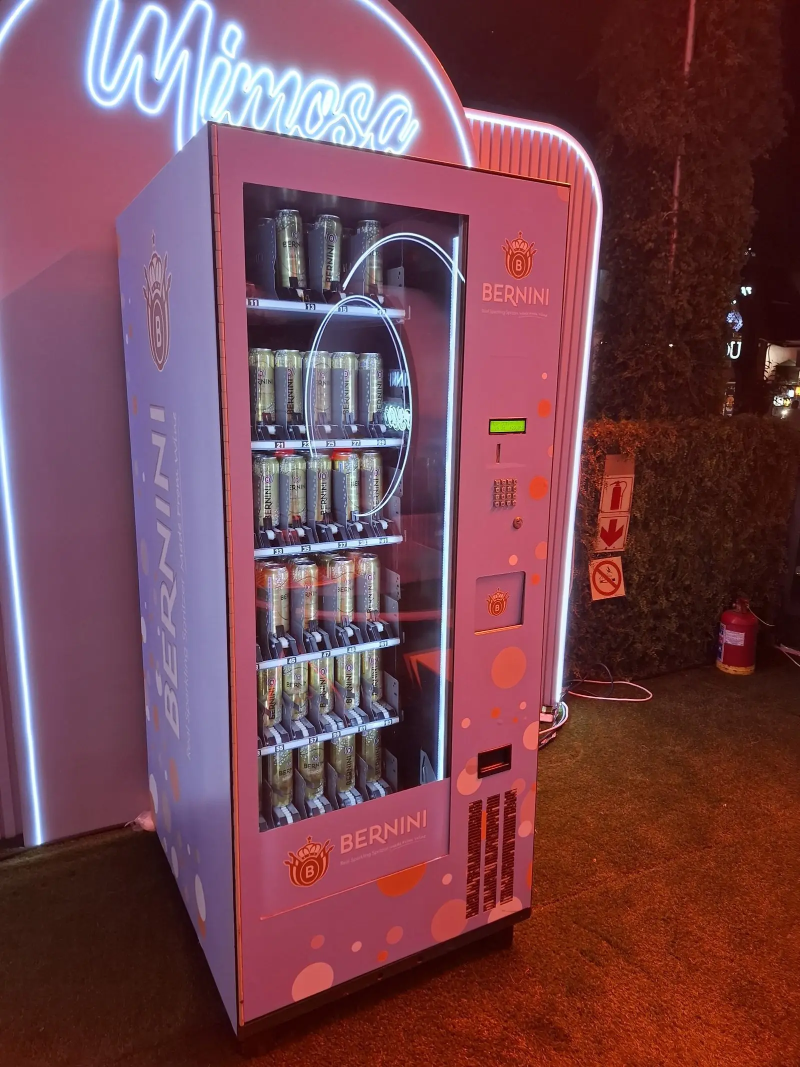 A Bernini-branded vending machine lit by pink neon at an evening venue activation