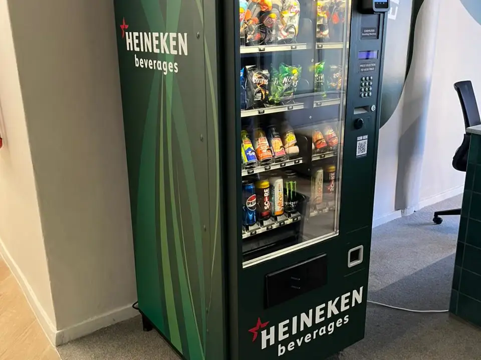 A standard combo vending machine vinyl-wrapped in dark green Heineken Beverages branding, stocked with snacks and cold drinks