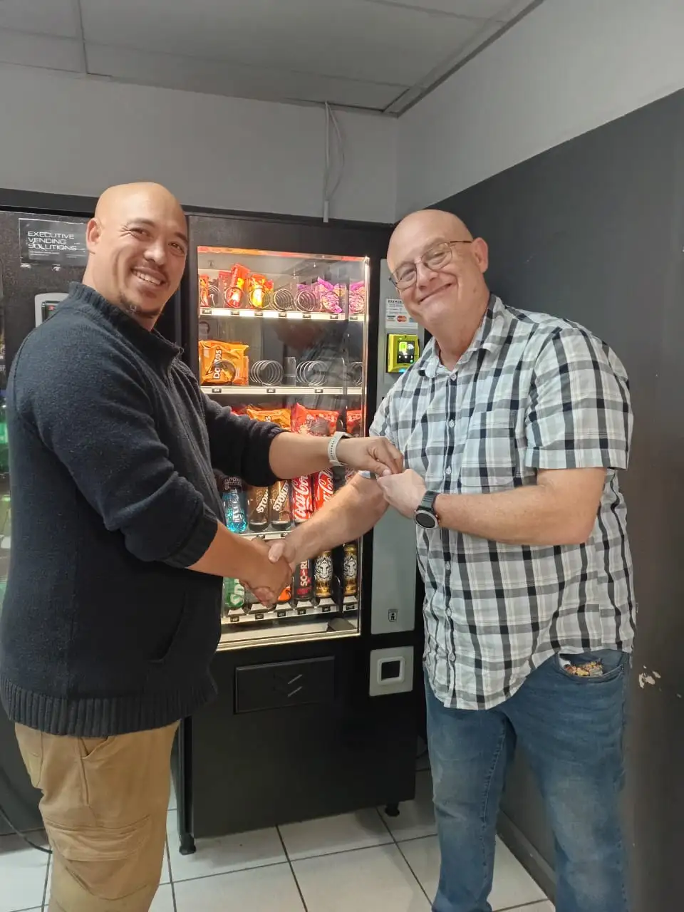 An IVS team member shaking hands with a client in front of their newly installed snack and cold drink vending machine