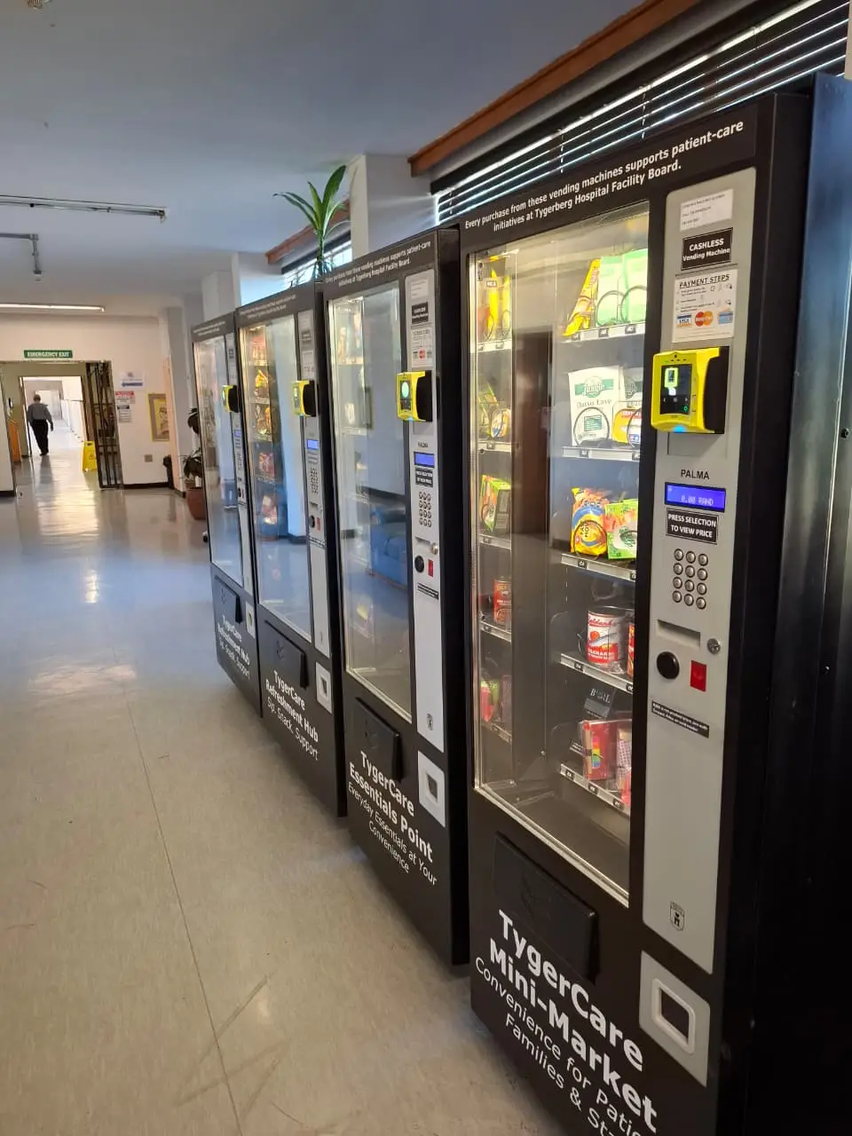 A row of vending machines along a hospital corridor, lit and stocked