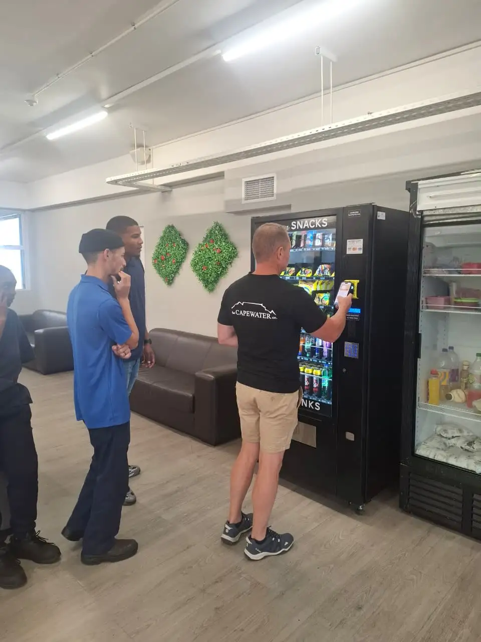 Office staff buying from a vending machine beside a water cooler
